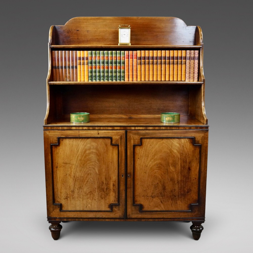 An antique Regency mahogany waterfall bookcase featuring open graduated shelves above a two-door lower cupboard resting on turned legs.