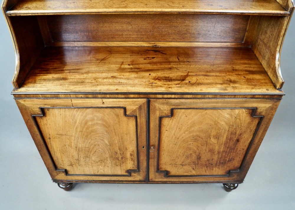 An antique Regency mahogany waterfall bookcase featuring open graduated shelves above a two-door lower cupboard resting on turned legs. View III