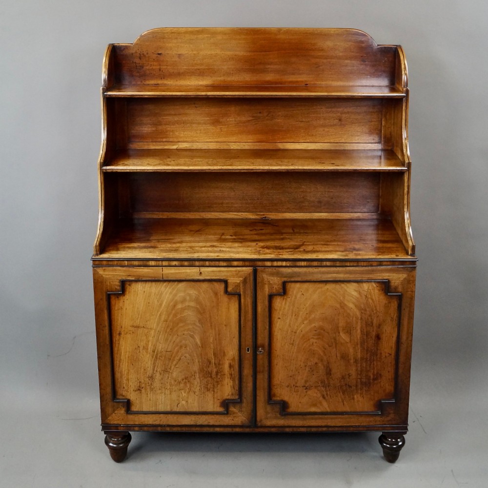 An antique Regency mahogany waterfall bookcase featuring open graduated shelves above a two-door lower cupboard resting on turned legs. View V