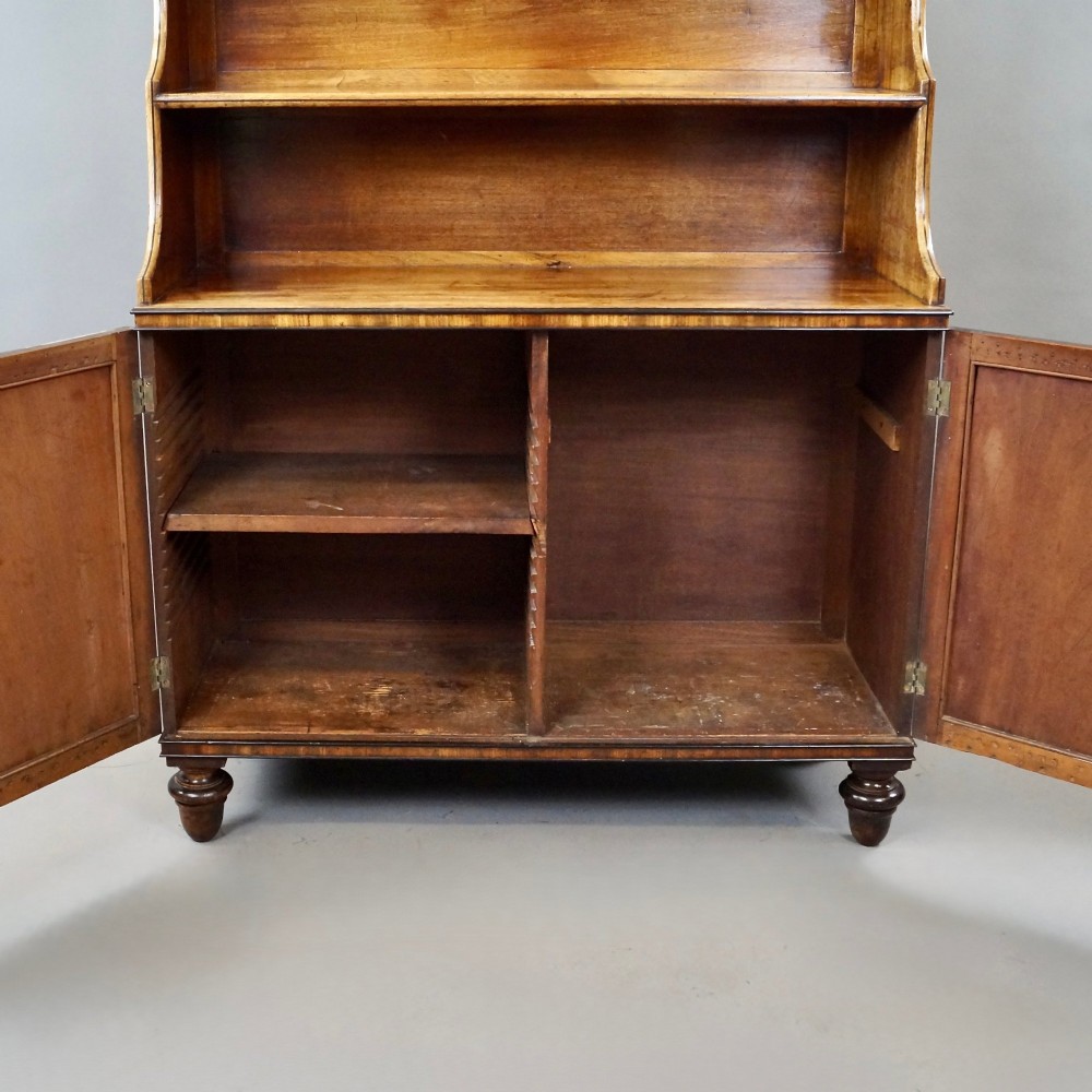An antique Regency mahogany waterfall bookcase featuring open graduated shelves above a two-door lower cupboard resting on turned legs. View VI