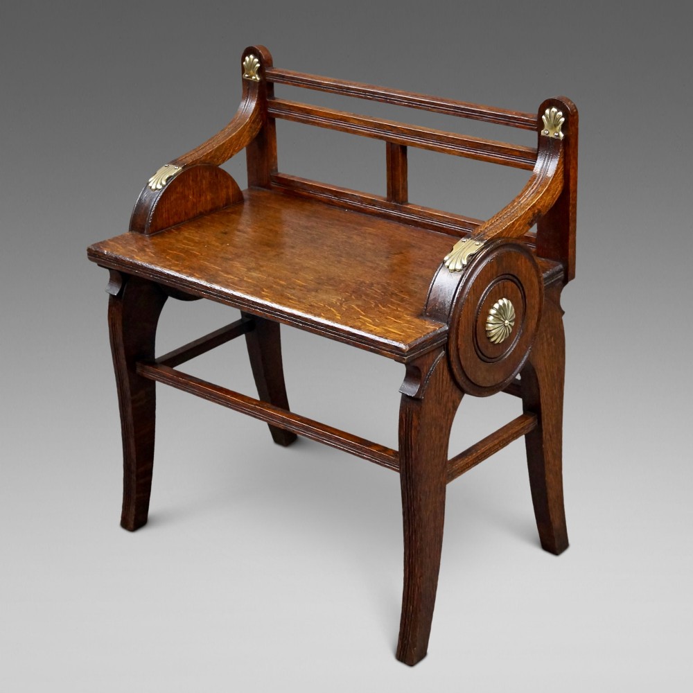 An antique solid oak hall bench featuring curved armrests with circular side panels and decorative brass shell mounts.