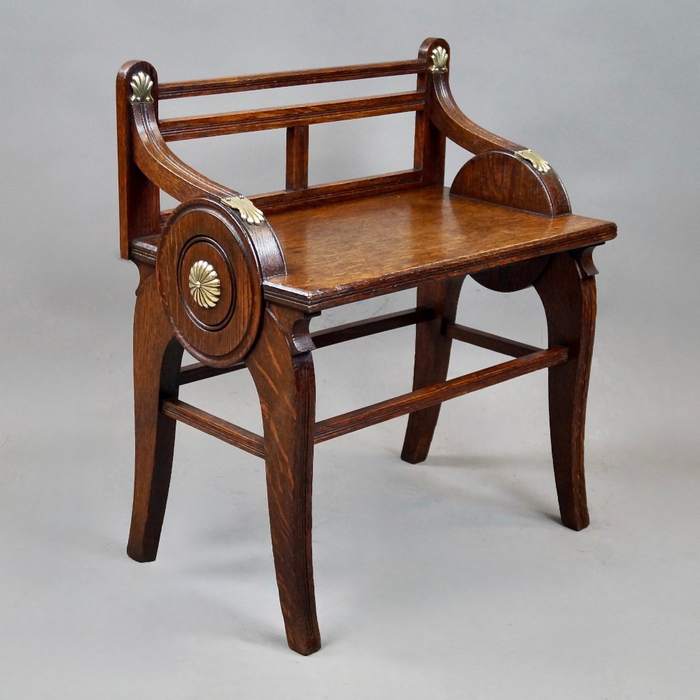 An antique solid oak hall bench featuring curved armrests with circular side panels and decorative brass shell mounts. View II