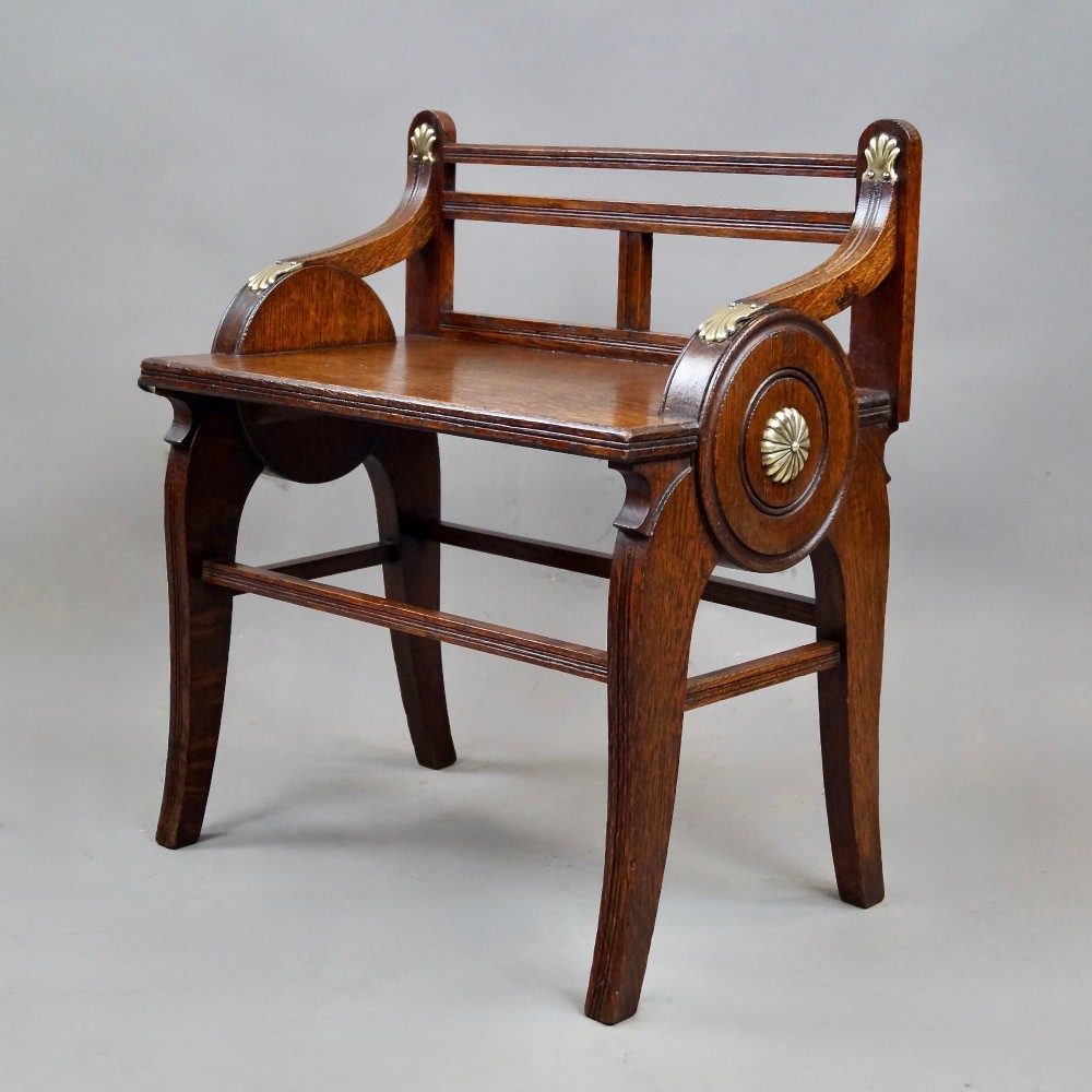 An antique solid oak hall bench featuring curved armrests with circular side panels and decorative brass shell mounts. View III