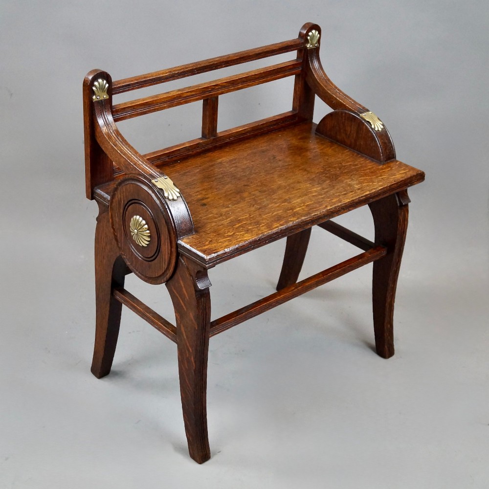 An antique solid oak hall bench featuring curved armrests with circular side panels and decorative brass shell mounts. View IV