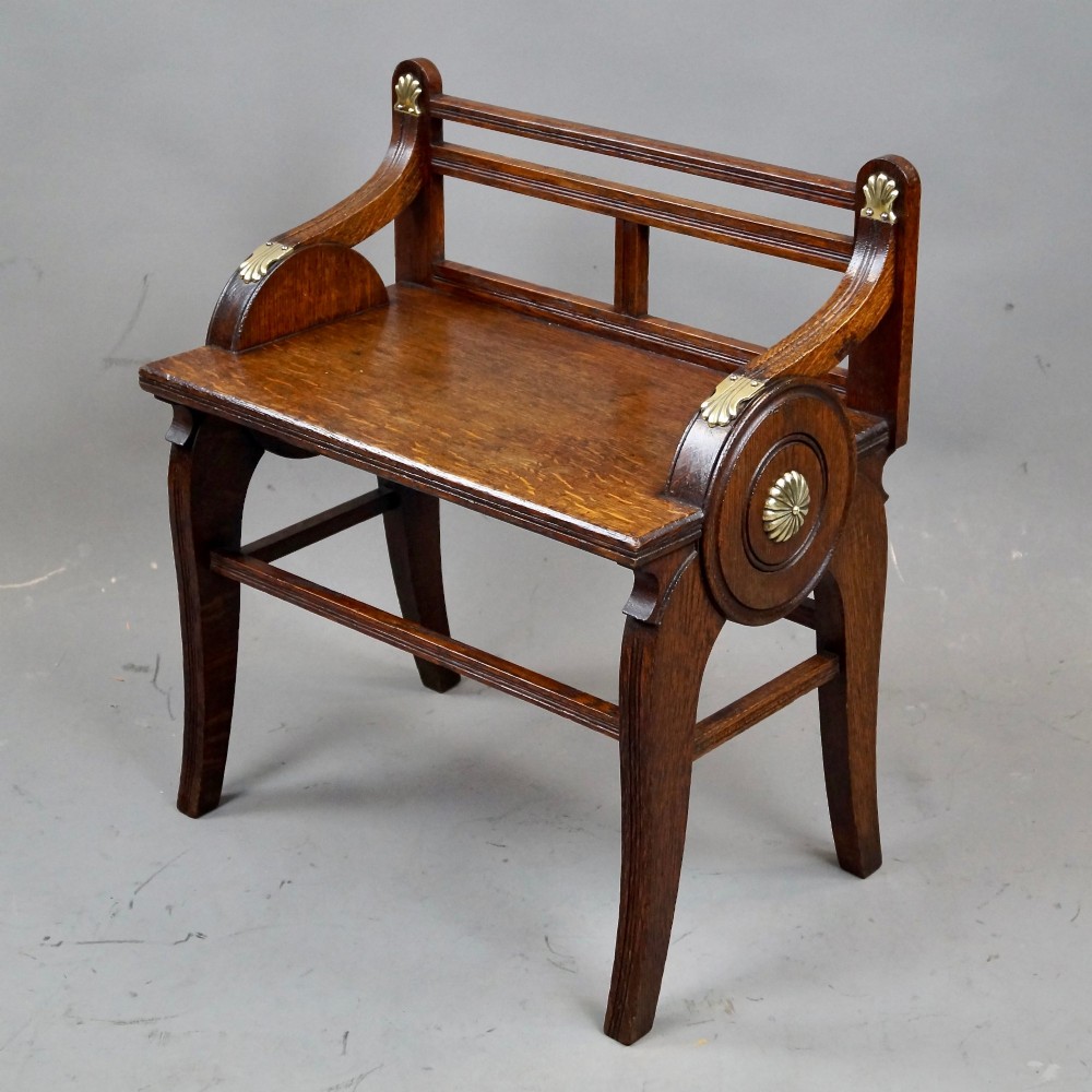 An antique solid oak hall bench featuring curved armrests with circular side panels and decorative brass shell mounts. View VI