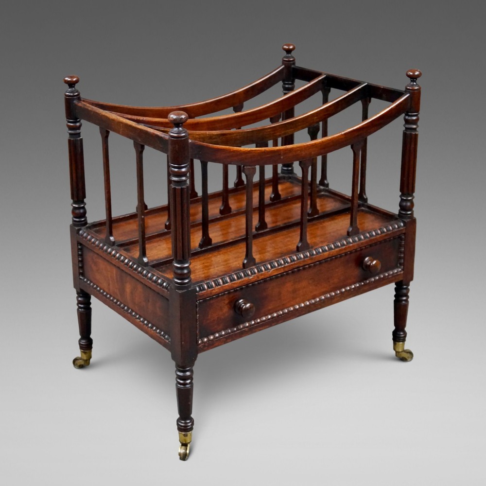 A William IV mahogany canterbury featuring four concave compartments with turned spindles, a single base drawer with wooden knobs, and turned legs on brass castors.