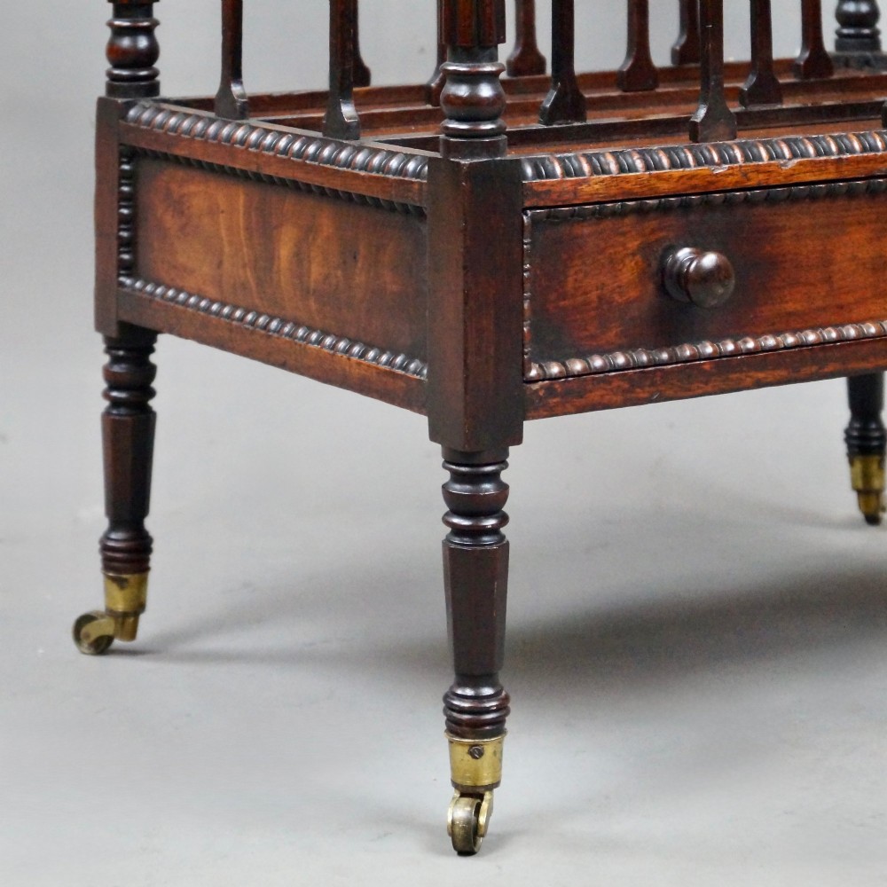 A William IV mahogany canterbury featuring four concave compartments with turned spindles, a single base drawer with wooden knobs, and turned legs on brass castors. View IV