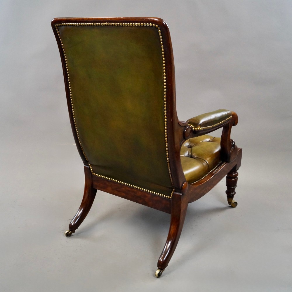 A William IV reclining armchair upholstered in deep-buttoned olive green leather with a mahogany frame, scroll arms, and brass castors. View V