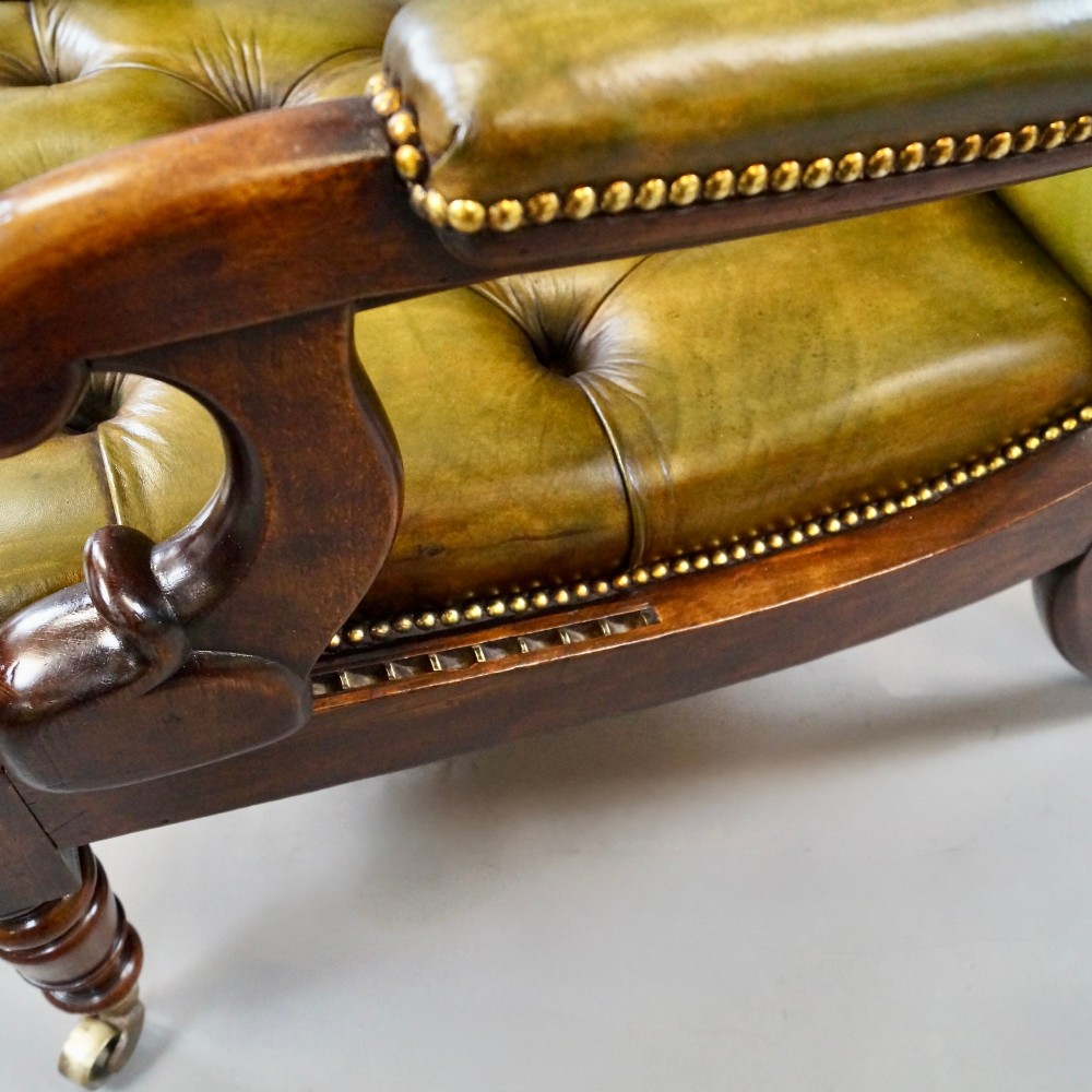 A William IV reclining armchair upholstered in deep-buttoned olive green leather with a mahogany frame, scroll arms, and brass castors. View VI