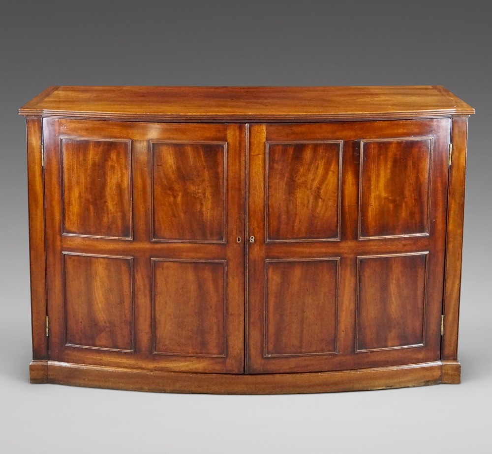 A George III bow-fronted mahogany storage cupboard featuring double doors with rectangular moulded panels.