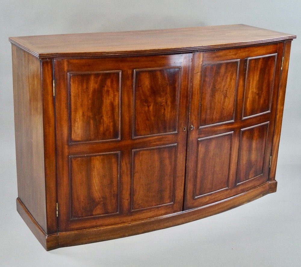 A George III bow-fronted mahogany storage cupboard featuring double doors with rectangular moulded panels. View II
