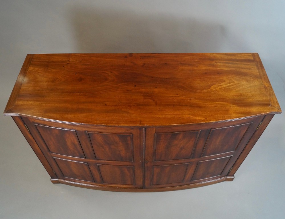 A George III bow-fronted mahogany storage cupboard featuring double doors with rectangular moulded panels. View III
