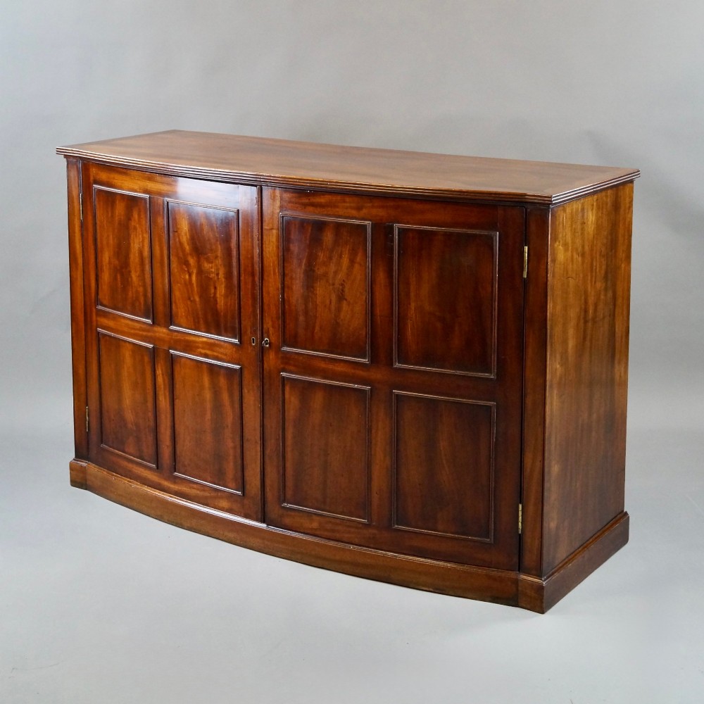 A George III bow-fronted mahogany storage cupboard featuring double doors with rectangular moulded panels. View IV