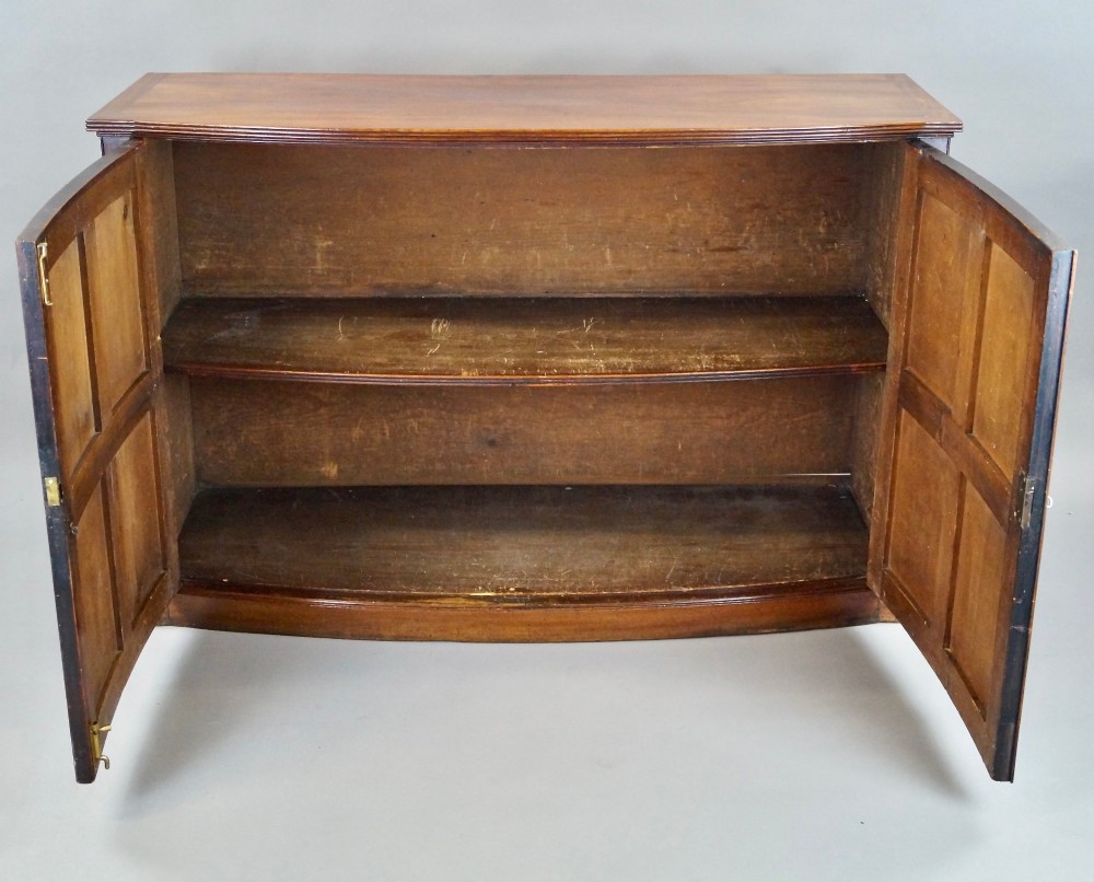 A George III bow-fronted mahogany storage cupboard featuring double doors with rectangular moulded panels. View V