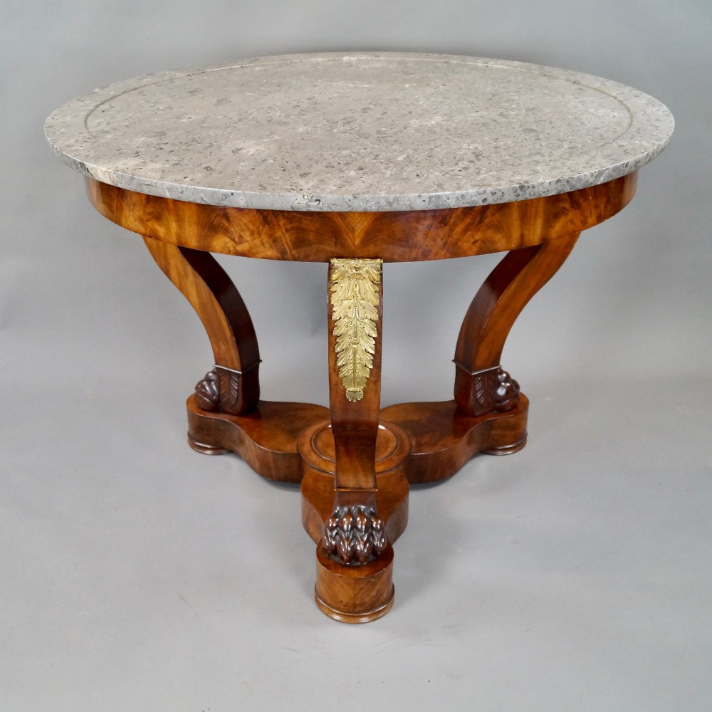 A circular French Empire mahogany gueridon table featuring a grey marble top, gilt bronze mounts, curved tripod legs, and carved lion paw feet on a plinth base. View V