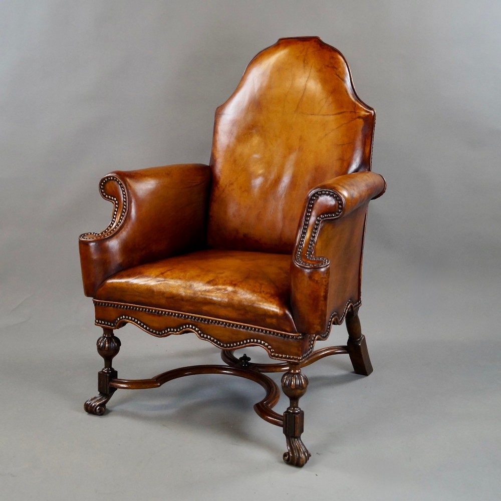 An 18th-century style tan leather armchair with brass stud trimming, scrolled arms, a shaped backrest, and carved walnut legs with a curved stretcher. View II