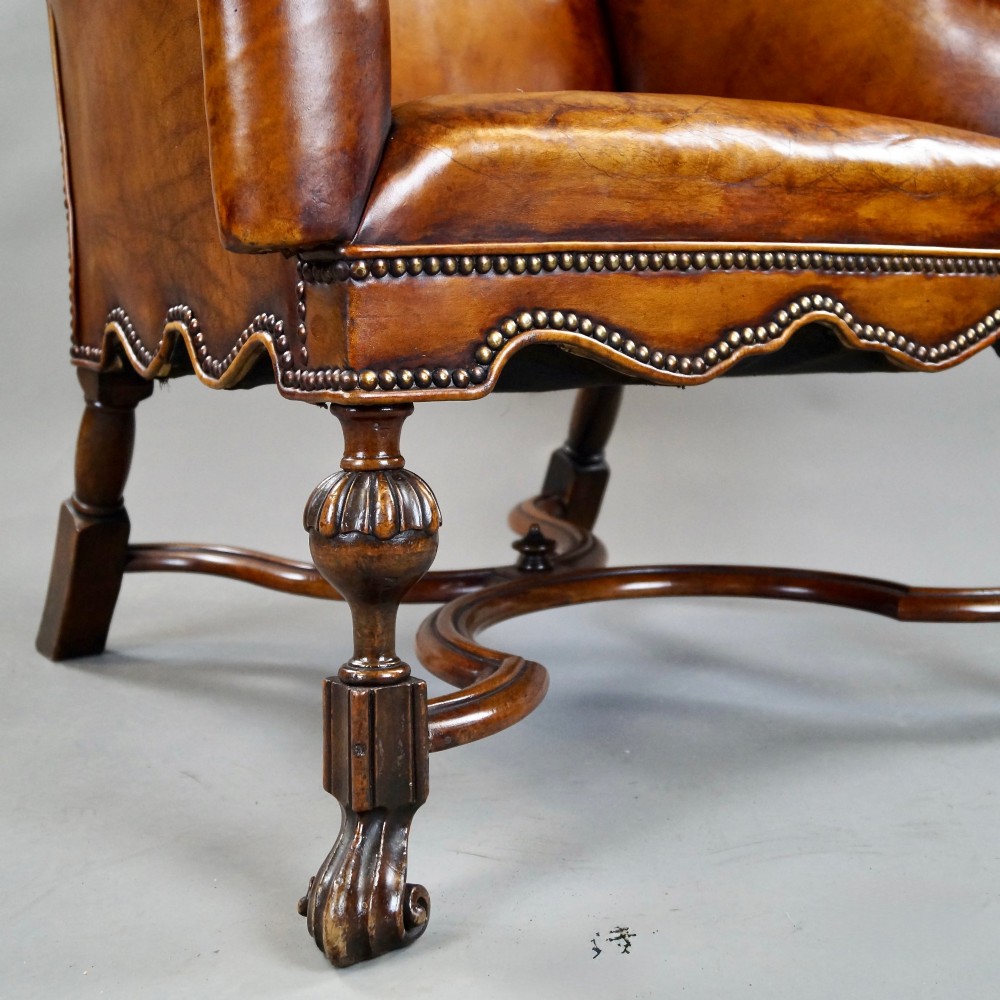 An 18th-century style tan leather armchair with brass stud trimming, scrolled arms, a shaped backrest, and carved walnut legs with a curved stretcher. View IV