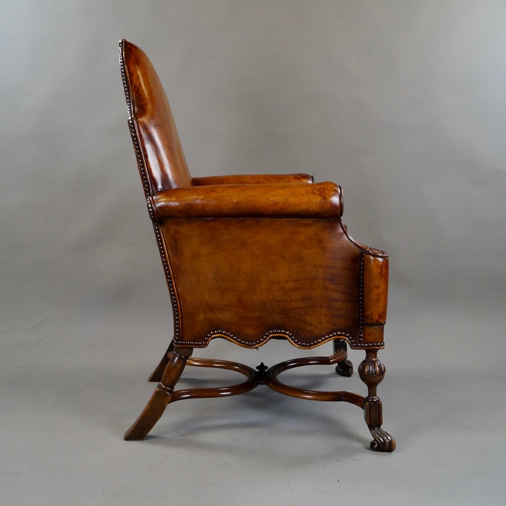 An 18th-century style tan leather armchair with brass stud trimming, scrolled arms, a shaped backrest, and carved walnut legs with a curved stretcher. View V