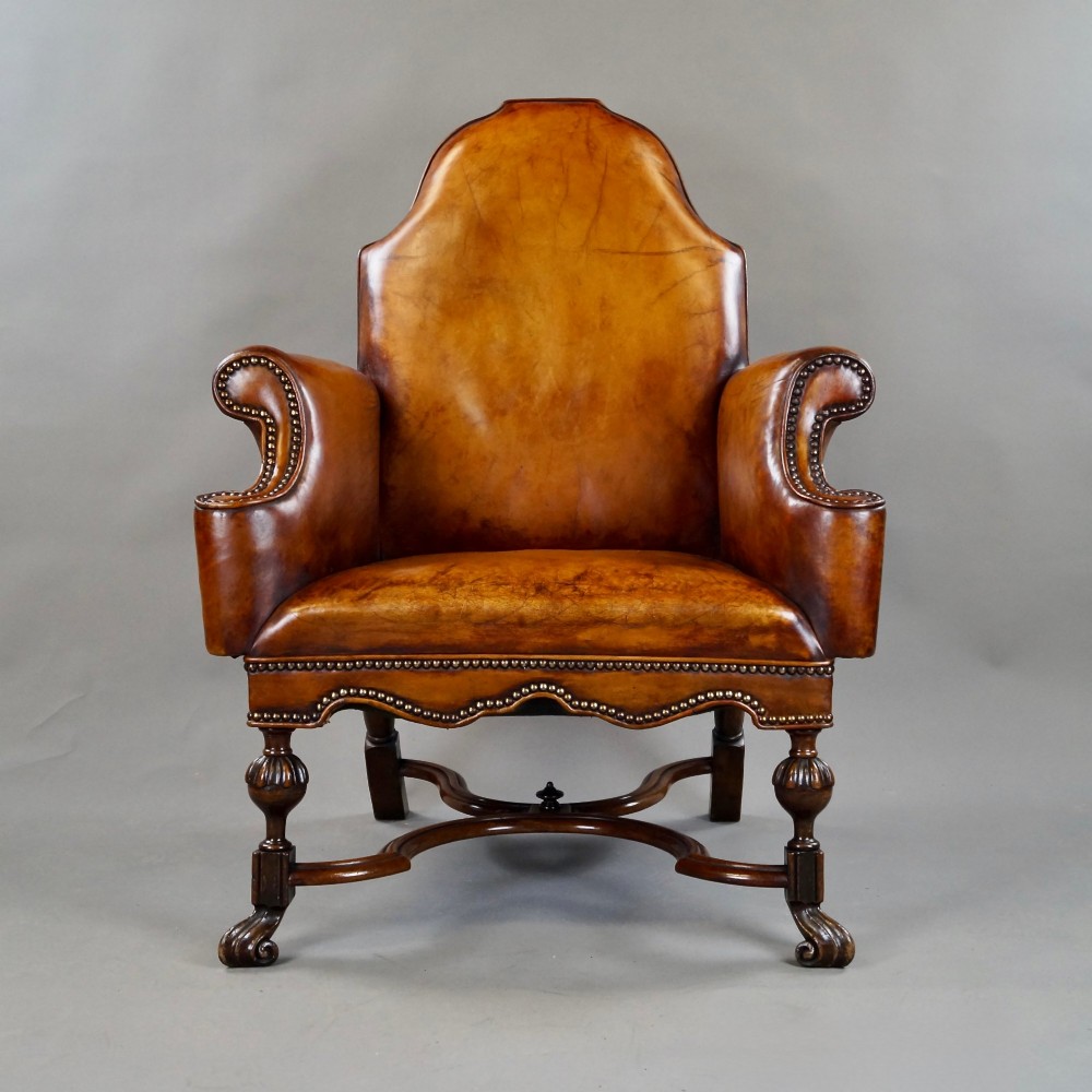 An 18th-century style tan leather armchair with brass stud trimming, scrolled arms, a shaped backrest, and carved walnut legs with a curved stretcher. View VI