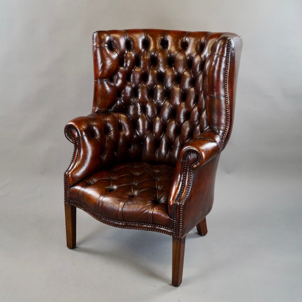 A chestnut brown leather wingback armchair featuring deep button tufting, brass stud detailing along the borders, and straight wooden legs. View II