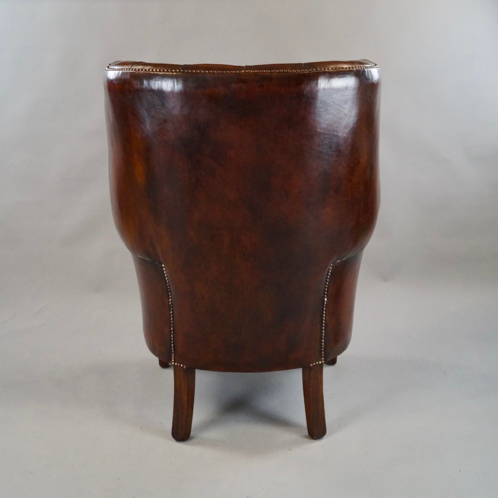 A chestnut brown leather wingback armchair featuring deep button tufting, brass stud detailing along the borders, and straight wooden legs. View IV
