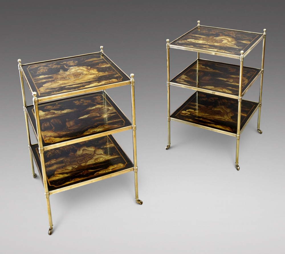 A pair of three-tiered brass etagere side tables featuring black lacquered shelves decorated with gold chinoiserie landscape scenes.
