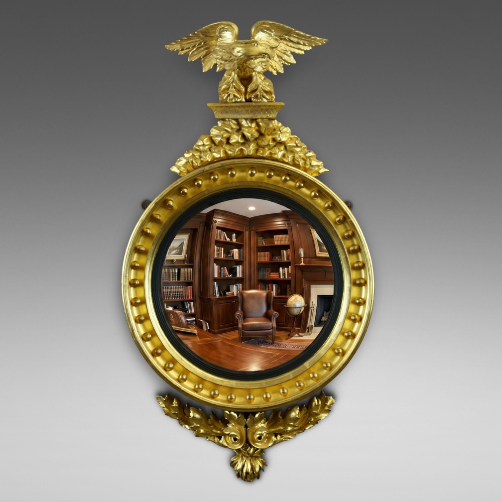 A circular Regency giltwood convex mirror framed with ball ornaments, crowned with an eagle cresting, and supported by carved acanthus leaf decoration at the base.