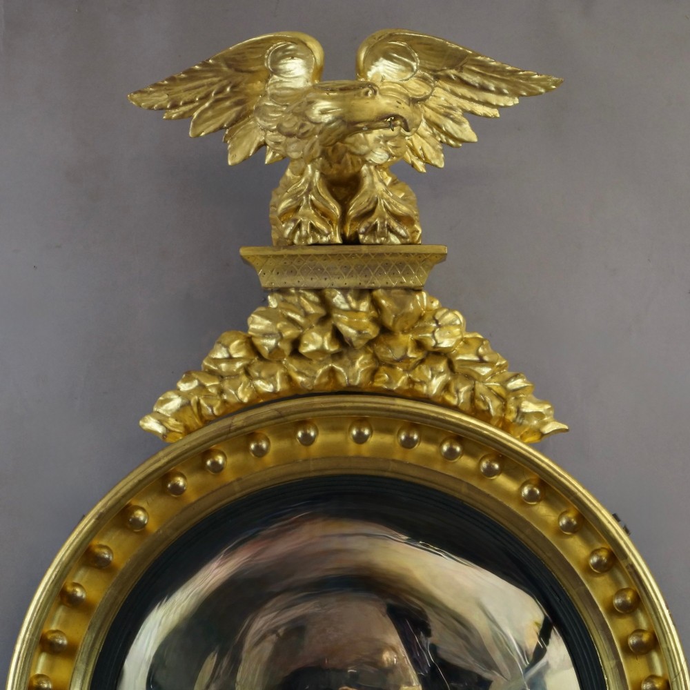 A circular Regency giltwood convex mirror framed with ball ornaments, crowned with an eagle cresting, and supported by carved acanthus leaf decoration at the base. View II