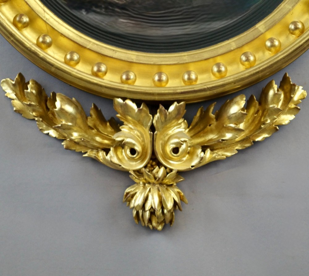 A circular Regency giltwood convex mirror framed with ball ornaments, crowned with an eagle cresting, and supported by carved acanthus leaf decoration at the base. View III