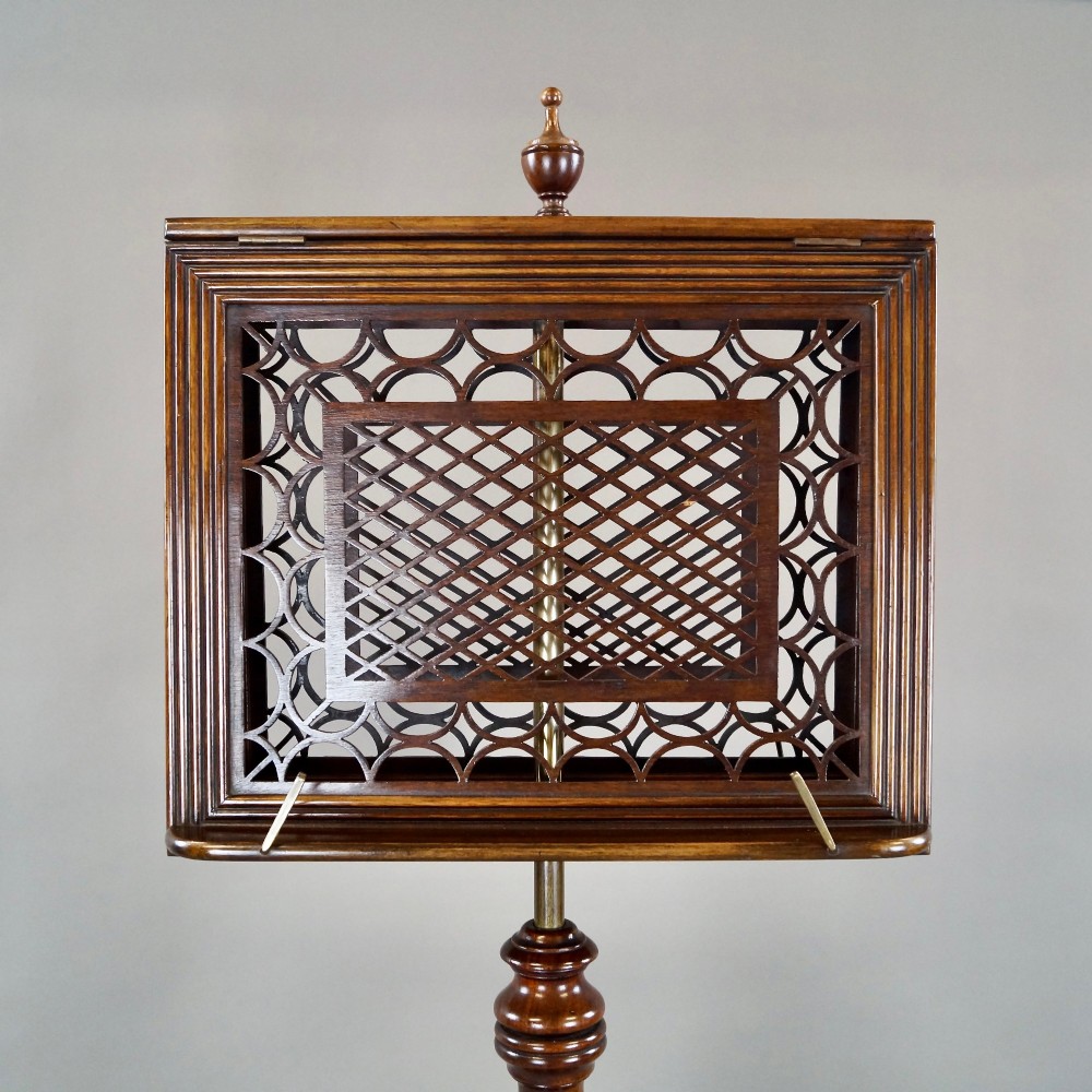 An antique mahogany duet music stand featuring a double-sided fretted lattice rest, brass adjustment mechanism, turned stem, and tripod base with castors. View II