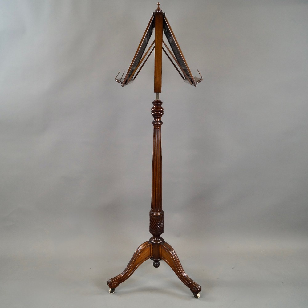 An antique mahogany duet music stand featuring a double-sided fretted lattice rest, brass adjustment mechanism, turned stem, and tripod base with castors. View V