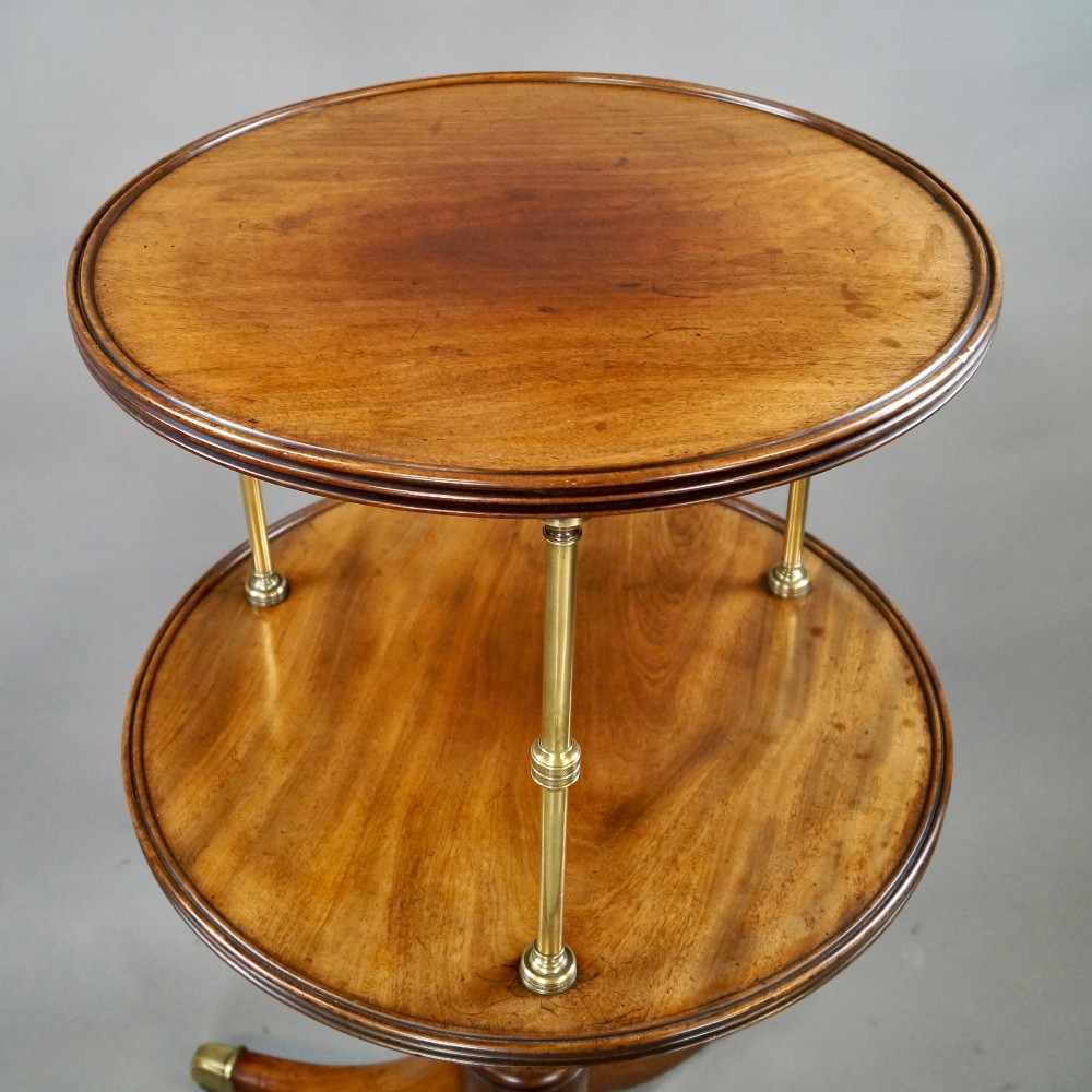 A two-tier Regency mahogany dumb waiter featuring circular surfaces separated by turned brass columns and supported on a turned central pedestal with tripod legs and brass castors. View II
