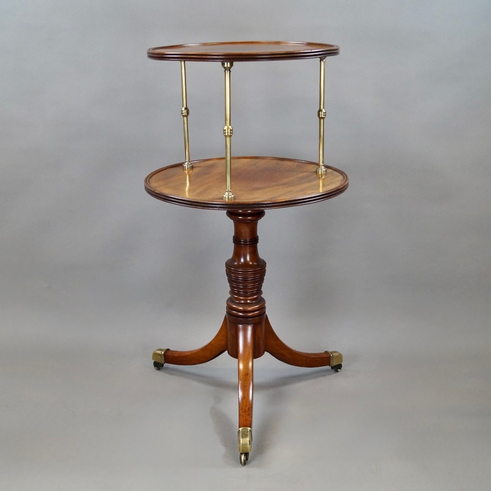 A two-tier Regency mahogany dumb waiter featuring circular surfaces separated by turned brass columns and supported on a turned central pedestal with tripod legs and brass castors. View VI