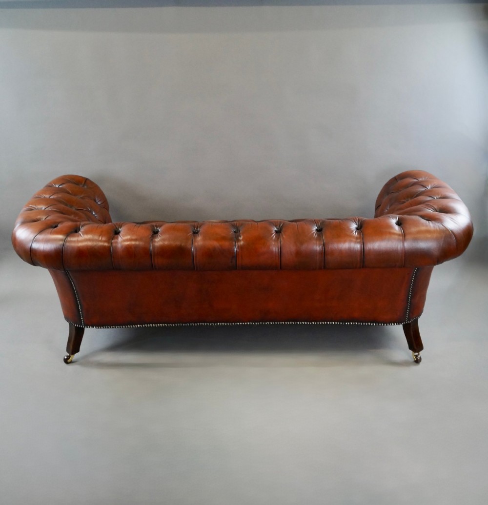 A Victorian deep-buttoned brown leather Chesterfield sofa featuring rolled arms, brass studding, and turned wooden legs. View II