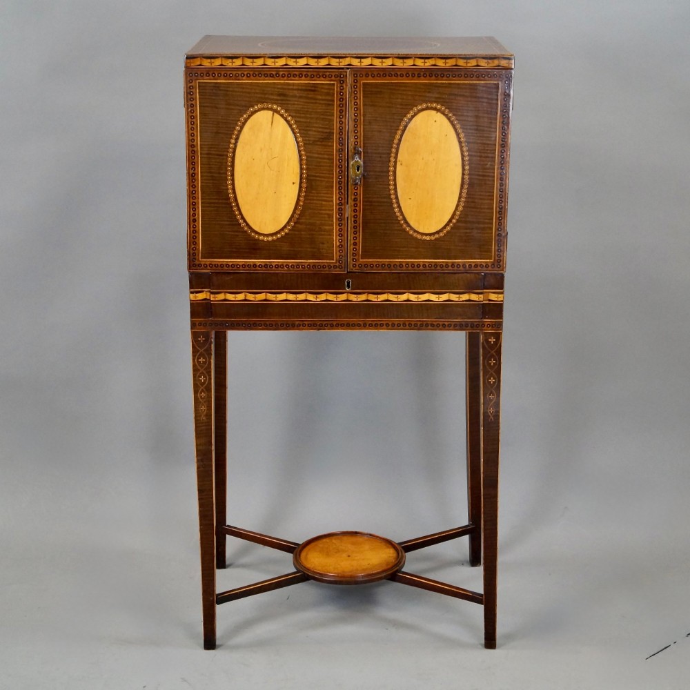 A Sheraton period harewood cabinet on stand featuring twin cupboard doors with oval satinwood inlays and slender tapered legs connected by a circular stretcher tray. View II