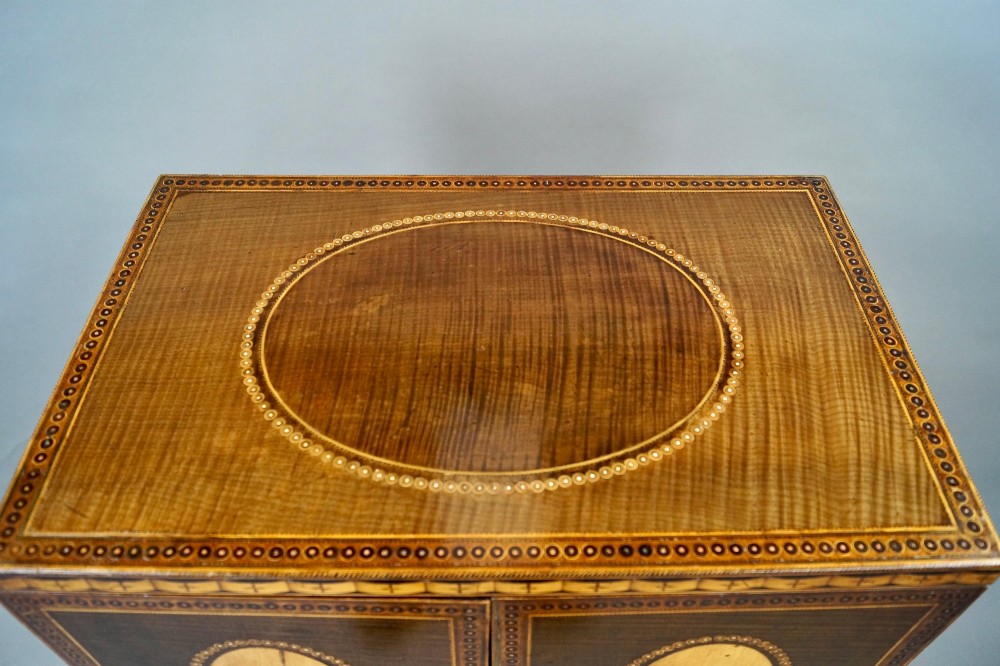 A Sheraton period harewood cabinet on stand featuring twin cupboard doors with oval satinwood inlays and slender tapered legs connected by a circular stretcher tray. View IV
