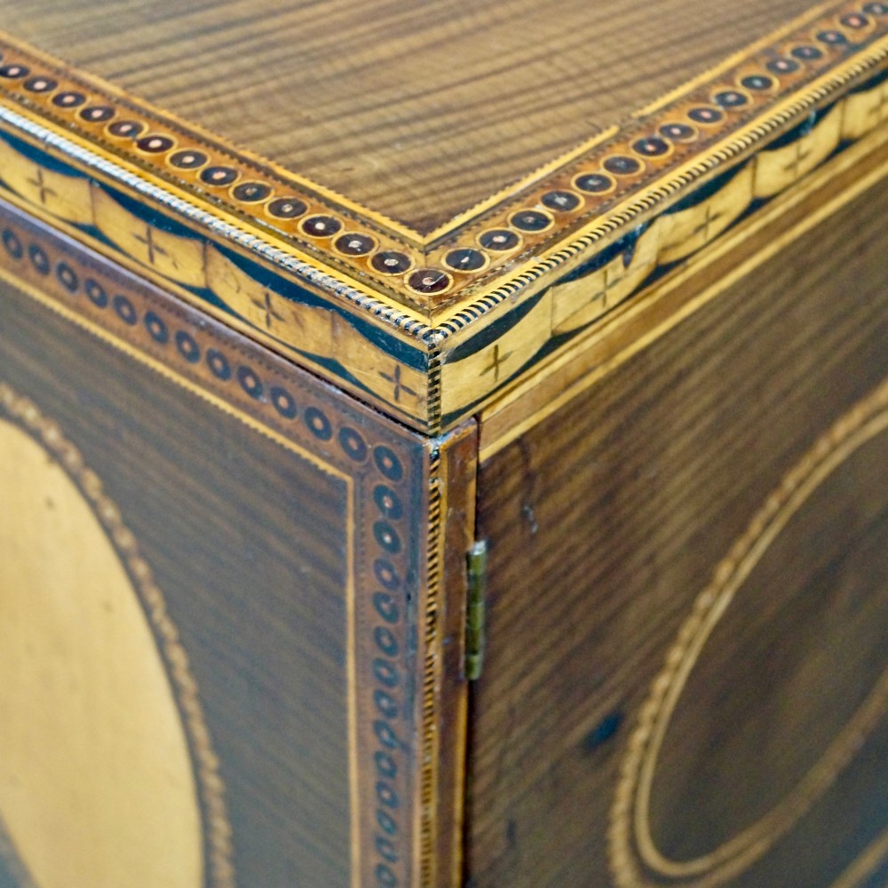A Sheraton period harewood cabinet on stand featuring twin cupboard doors with oval satinwood inlays and slender tapered legs connected by a circular stretcher tray. View VII