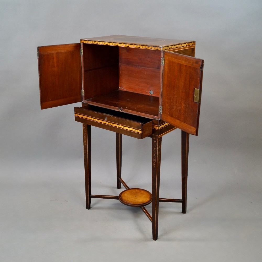 A Sheraton period harewood cabinet on stand featuring twin cupboard doors with oval satinwood inlays and slender tapered legs connected by a circular stretcher tray. View VIII