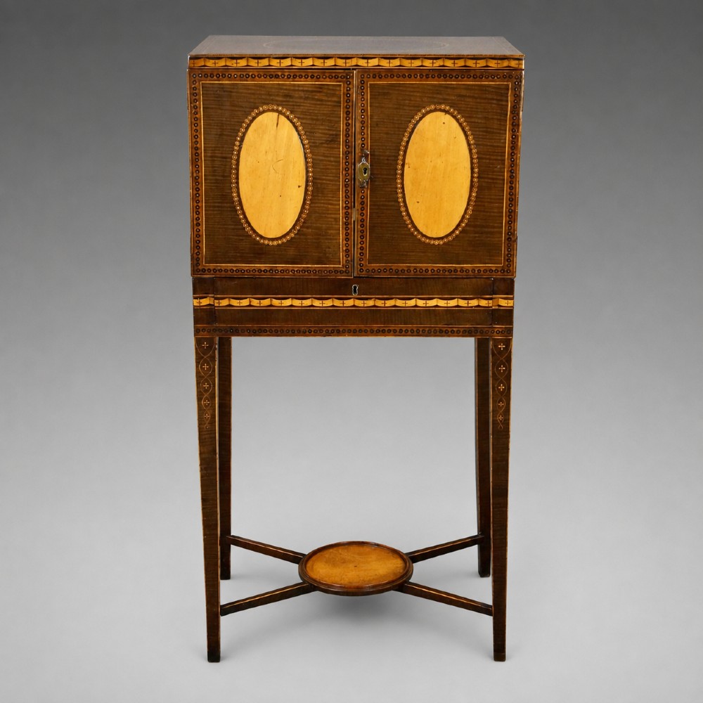 A late eighteenth-century Sheraton period harewood cabinet on stand featuring oval satinwood medallions, inlaid borders, slender square tapered legs, and a central stretcher tier. View II