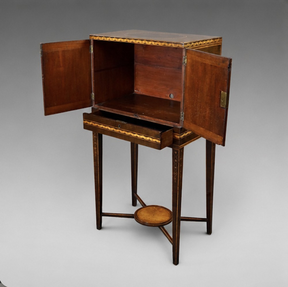 A late eighteenth-century Sheraton period harewood cabinet on stand featuring oval satinwood medallions, inlaid borders, slender square tapered legs, and a central stretcher tier. View V