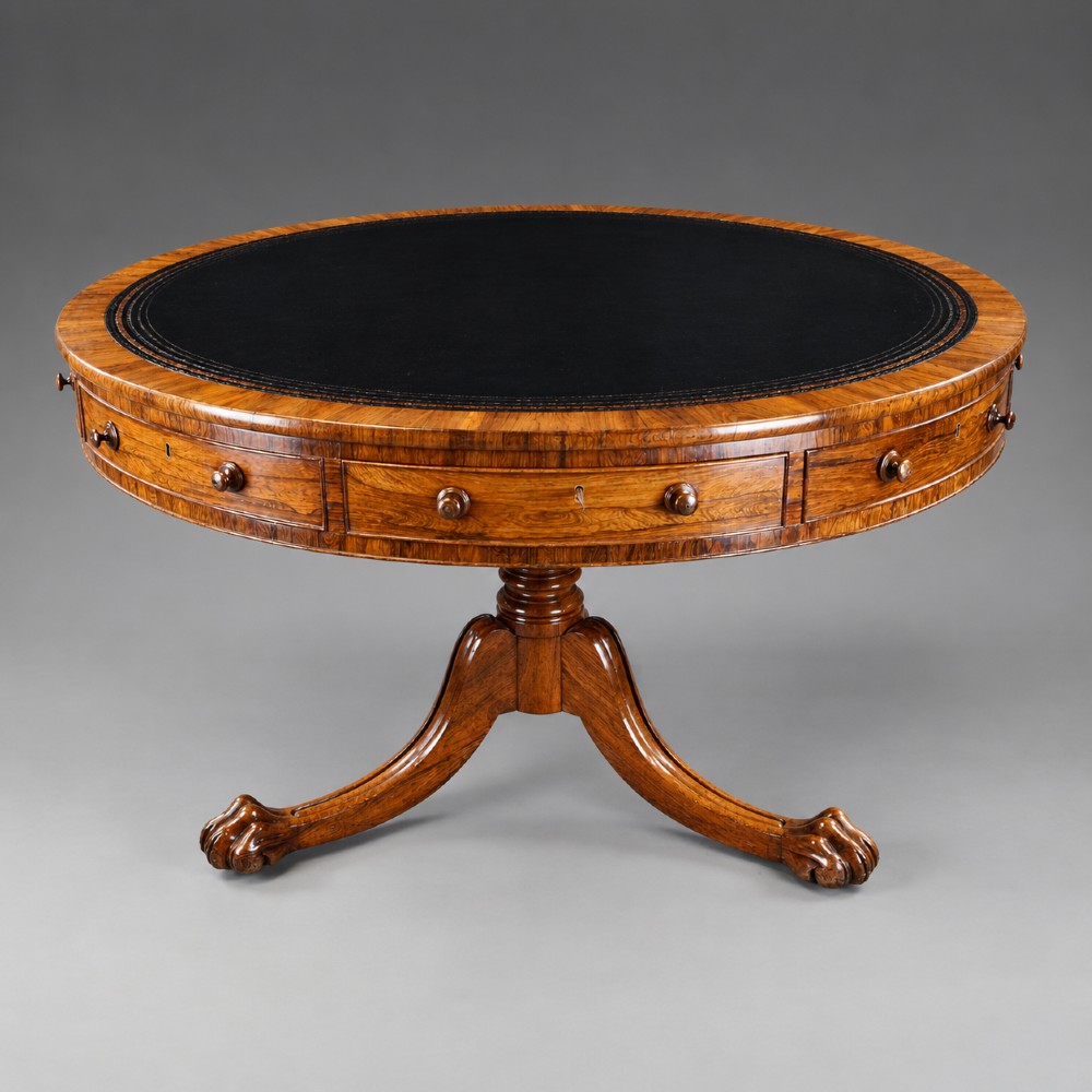 A circular Regency rosewood drum table featuring a black leather insert, perimeter drawers with turned knobs, and a central pedestal with splayed carved legs.