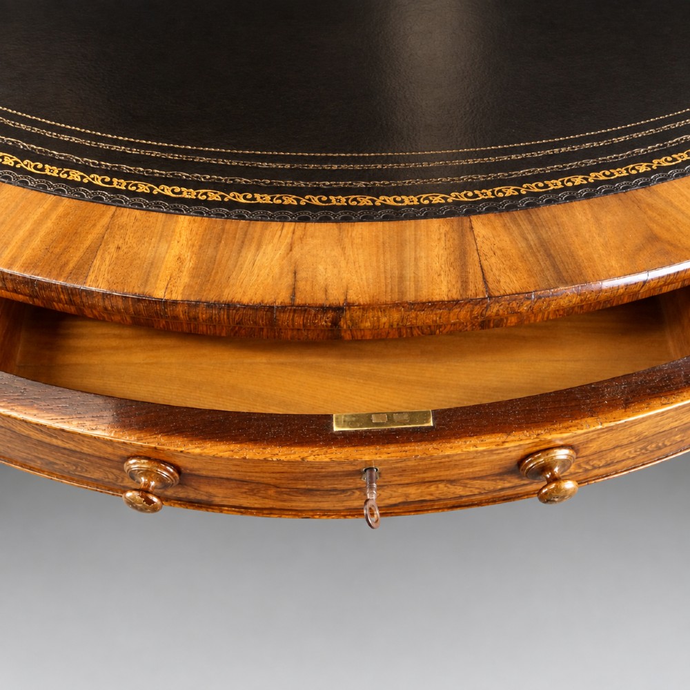 A circular Regency rosewood drum table featuring a black leather insert, perimeter drawers with turned knobs, and a central pedestal with splayed carved legs. View V