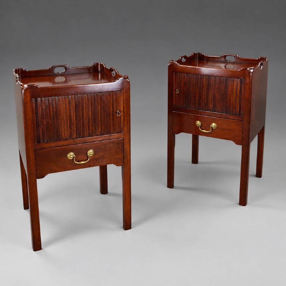 A pair of Georgian style mahogany bedside cupboards featuring top gallery trays with cut-out handles, slatted tambour doors, single lower drawers with brass handles, and square legs.