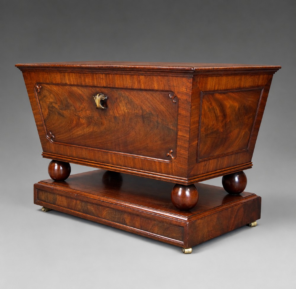 A Regency flame mahogany tapered wine cooler with a central brass escutcheon, supported by turned spherical feet and a rectangular plinth base. View II
