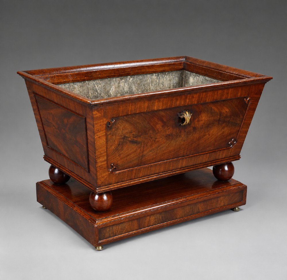 A Regency flame mahogany tapered wine cooler with a central brass escutcheon, supported by turned spherical feet and a rectangular plinth base. View III