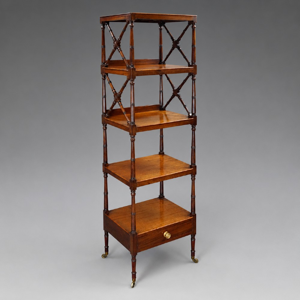 A tall George III mahogany four-tier whatnot featuring X-frame lattice sides on upper tiers, turned upright supports, a single drawer with a brass knob, and brass castors.