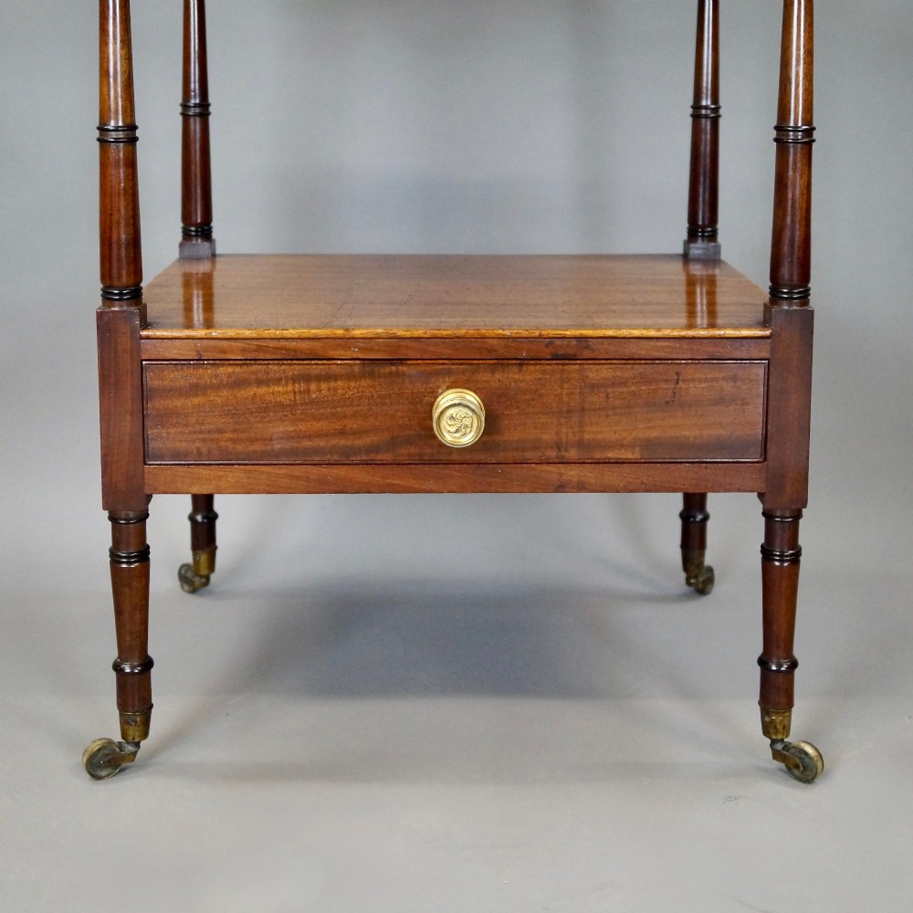 A tall George III mahogany four-tier whatnot featuring X-frame lattice sides on upper tiers, turned upright supports, a single drawer with a brass knob, and brass castors. View IV
