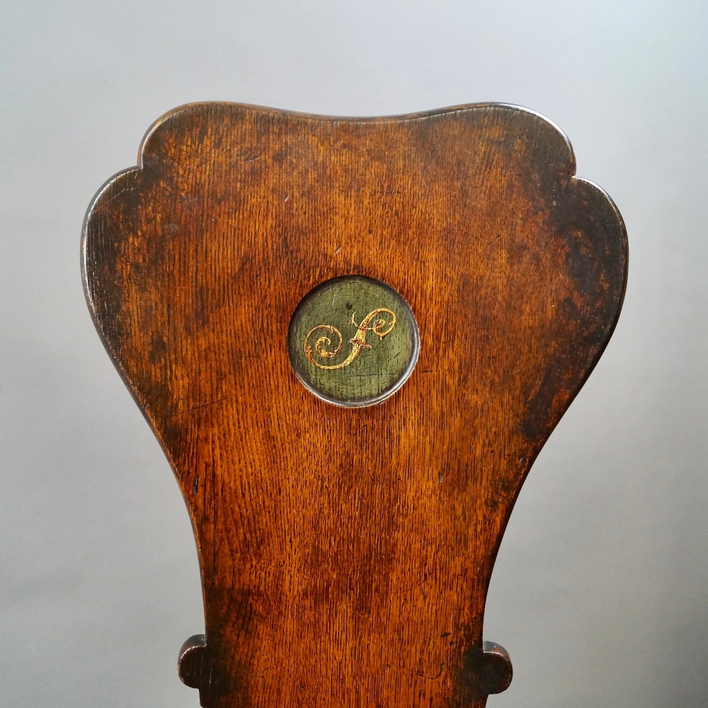 A pair of dark oak sgabello hall chairs featuring contoured seats, scroll-cut trestle bases, and shaped cartouche backrests with painted green and gold central roundels. View III