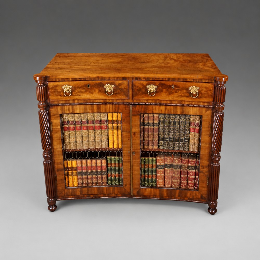 A William IV mahogany side cabinet featuring a concave front, two drawers with circular brass drop handles, and two lower mesh wire grille doors flanked by spiral-turned columns. View II