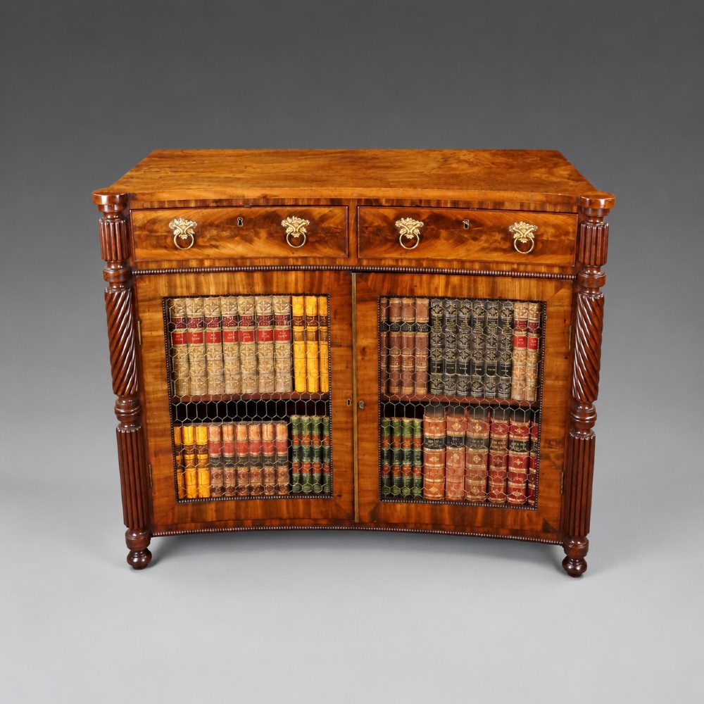 A William IV mahogany side cabinet featuring a concave front, two drawers with circular brass drop handles, and two lower mesh wire grille doors flanked by spiral-turned columns. View IV